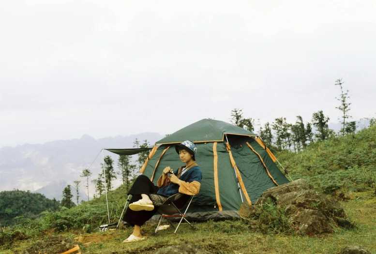 a man is sitting outside of a green tent