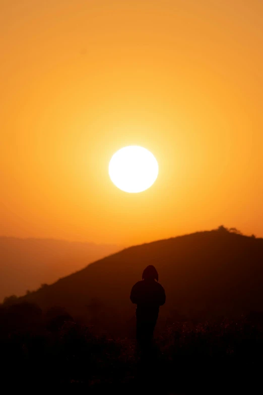 a person standing in the middle of a field with a sunset behind them