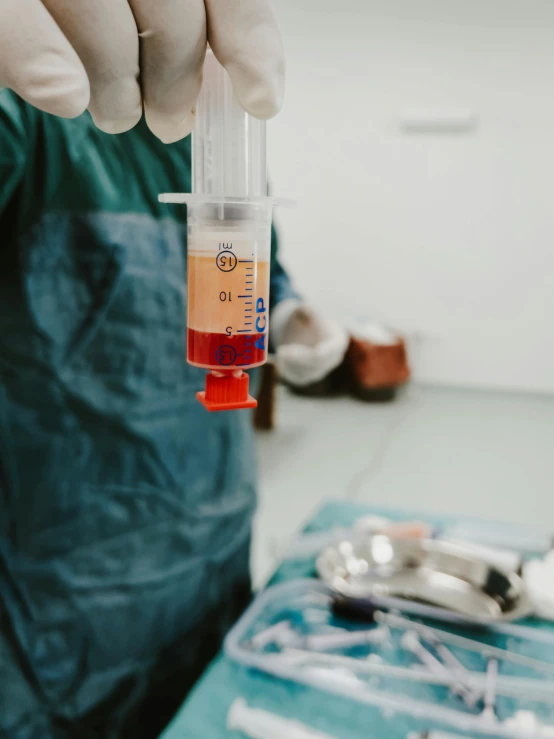 a person in blue holding a pipette with an orange liquid