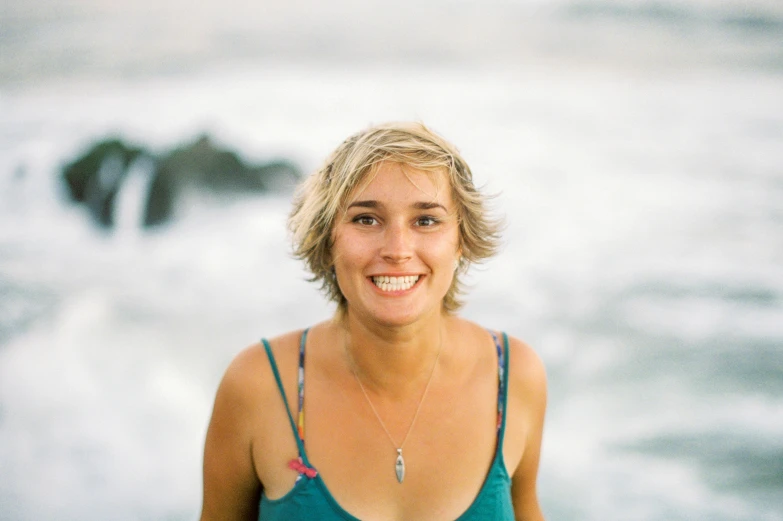 a smiling blonde woman in blue and black shirt standing next to the ocean