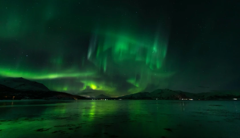 the bright green aurora bores above a body of water at night