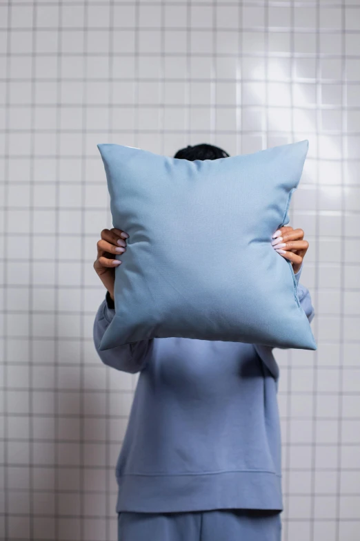 a woman holds up a blue pillow and has her face on the pillow