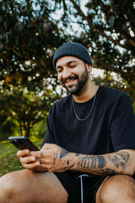 a bearded man with tattoos on his arm sitting on a bench looking at his cell phone