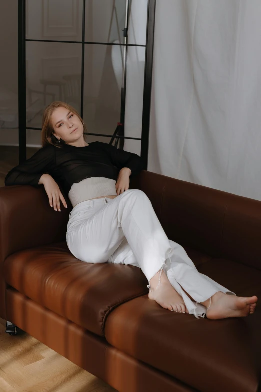 a woman in white pants and black top sitting on a couch