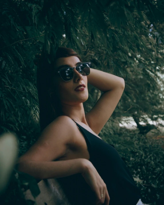 a beautiful young lady wearing glasses, leaning against a tree