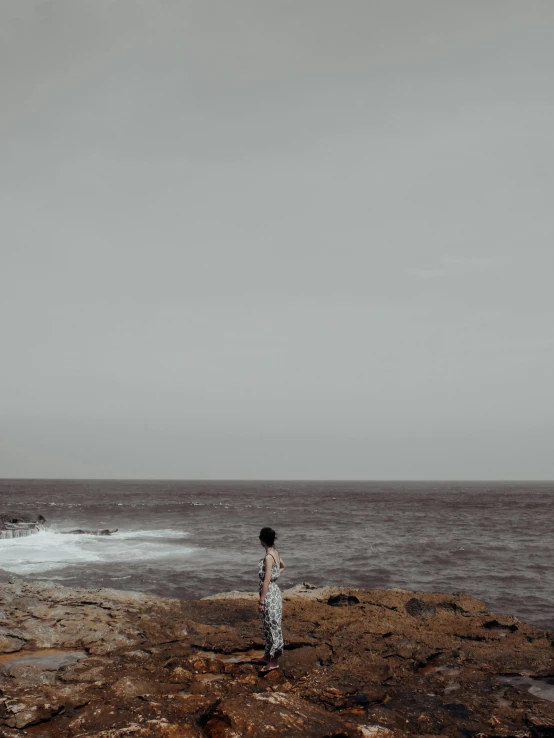 a woman is standing on rocks and looking at the water