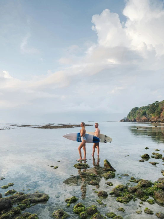 two men are standing in the water holding a surfboard