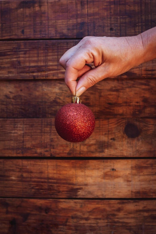 hand holding a red ornament on a wood background