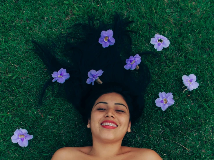 a woman lying in grass with flowers surrounding her