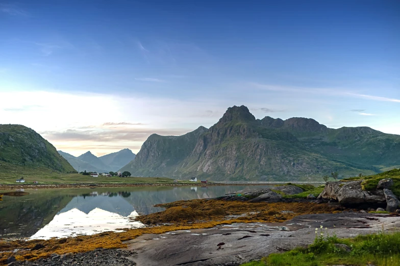 a mountain range with a body of water surrounded by grass and rock