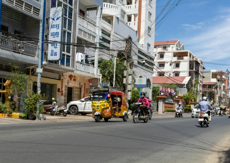 two motorcyclists ride down the street past tall buildings