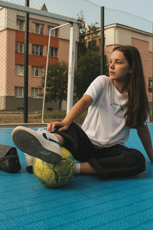 a woman sits on the ground with her foot resting on a soccer ball