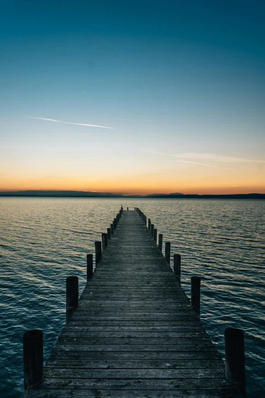 a large dock extends out to the ocean as a golden sunset