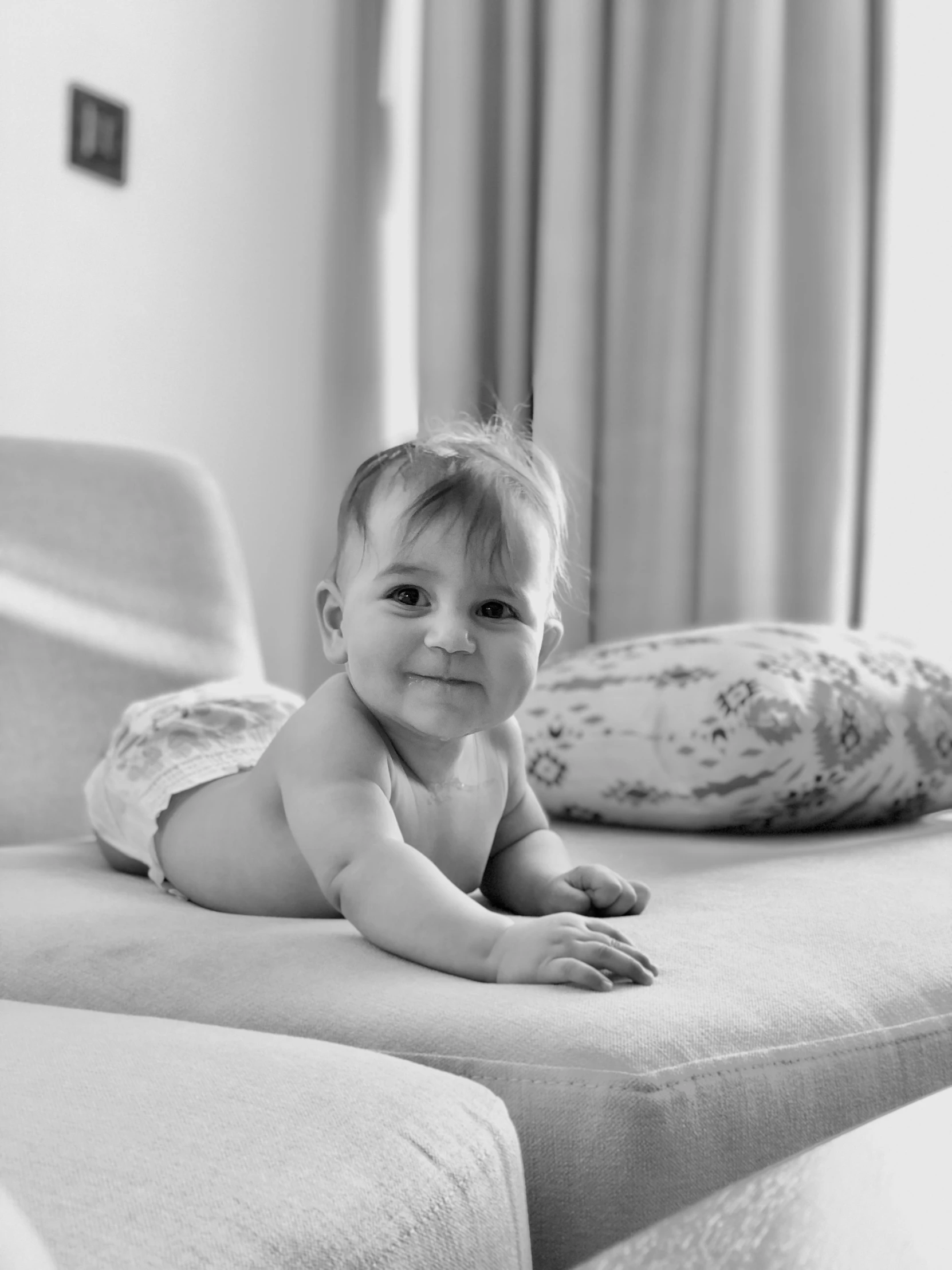 baby sitting on an ottoman with his arms and legs folded