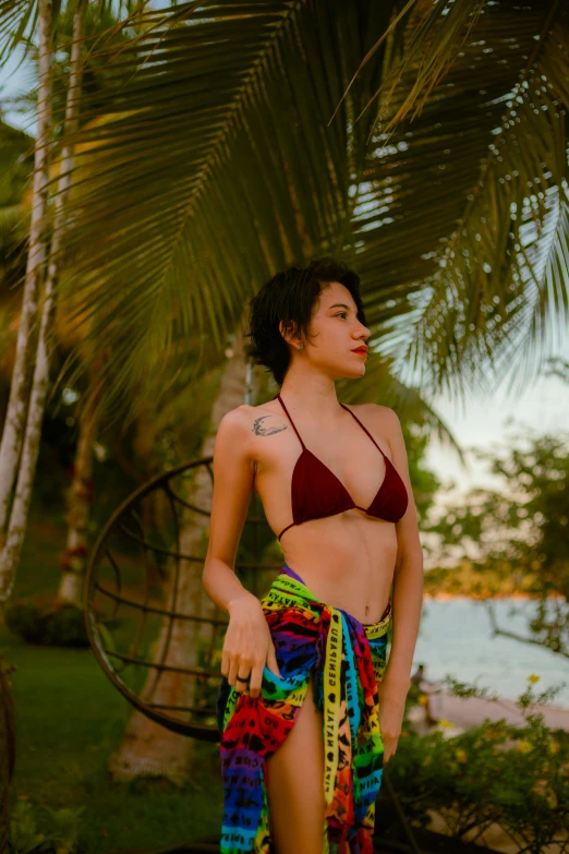 a young woman is standing next to a palm tree wearing a colorful bikini