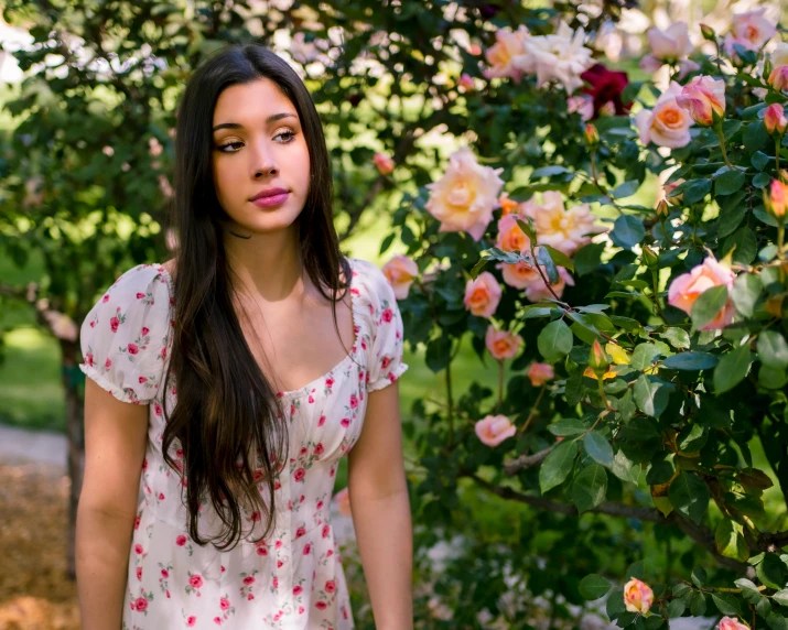 a beautiful woman stands in front of a pink rose bush