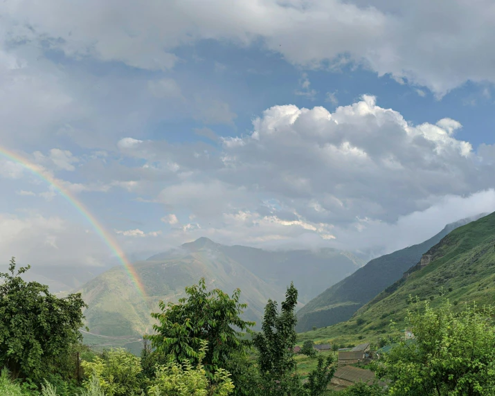 a rainbow appears over a green mountain range