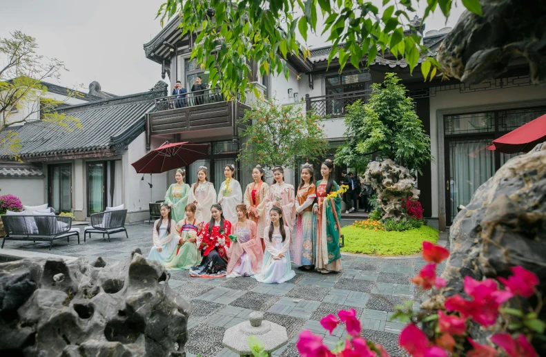 several women in long dresses and umbrellas stand outside of a house