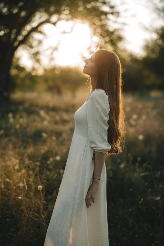 a young lady with long red hair standing in a field at sunset