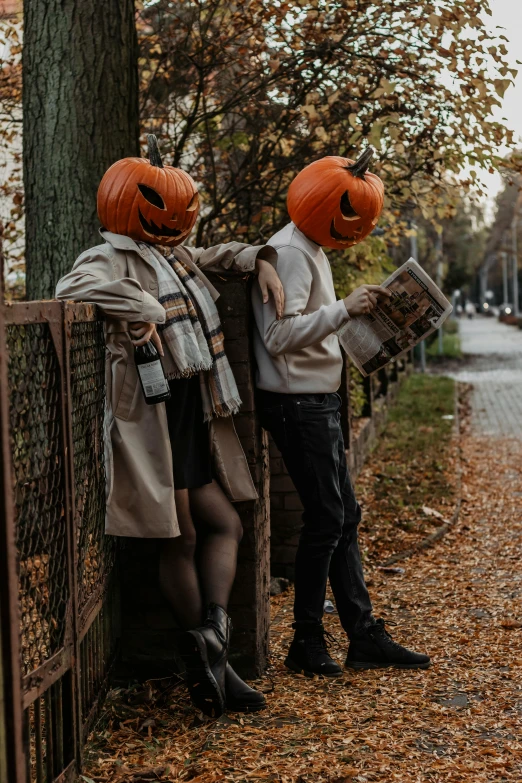 a couple wearing pumpkin hats standing next to a tree with their arms crossed