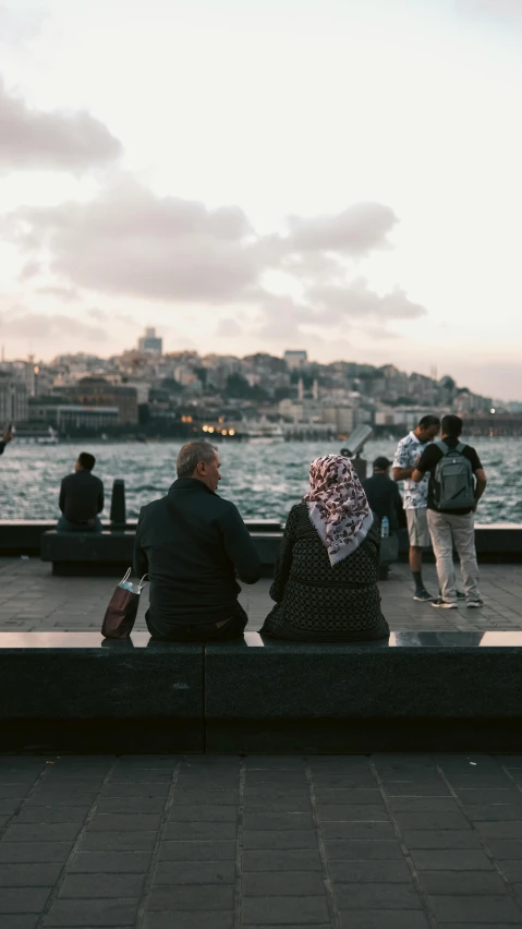 two people sit on the edge of a pier near the ocean