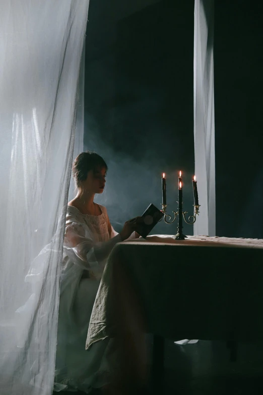 a woman in white dress sitting by window with lighted candles