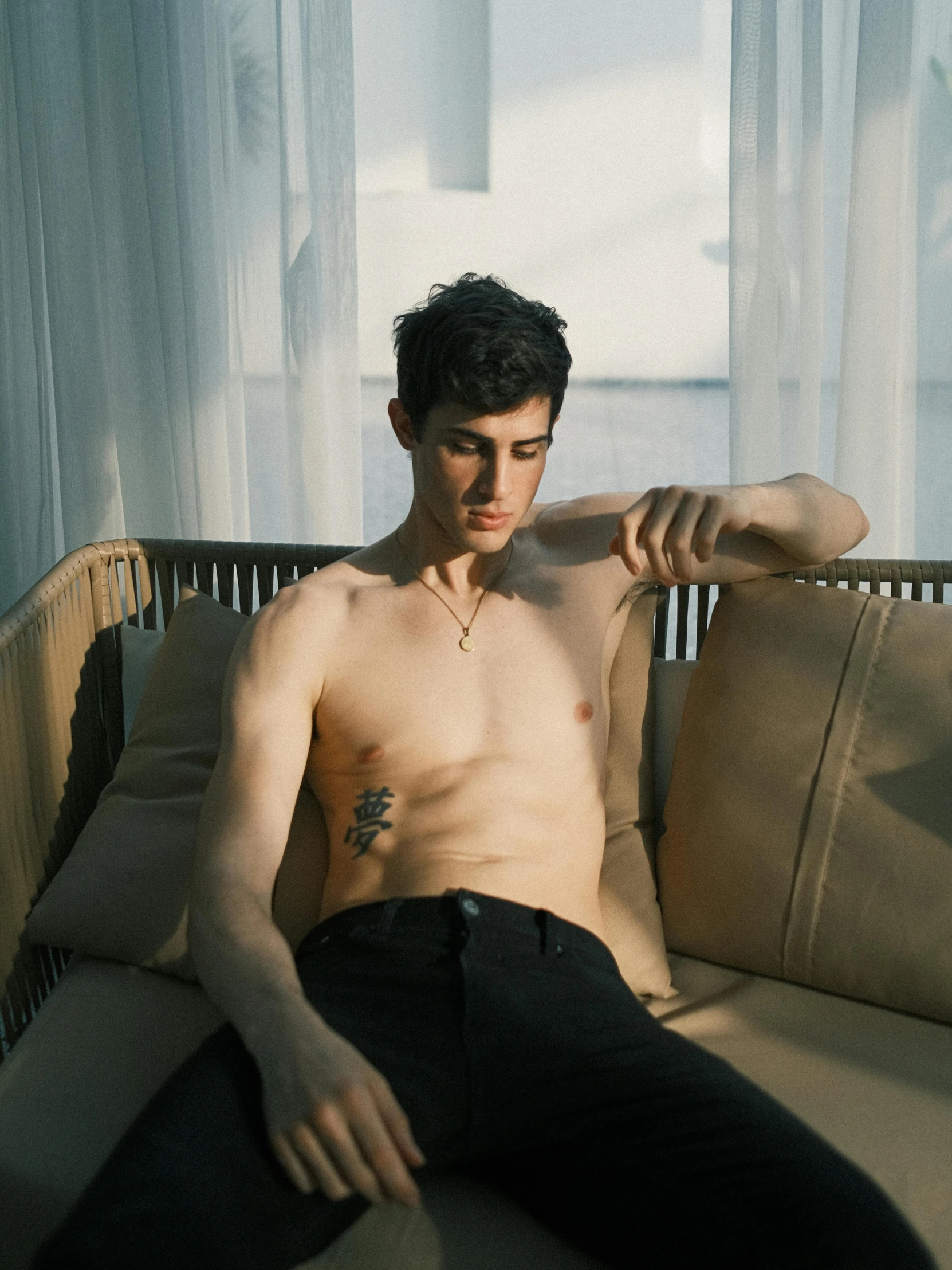 a shirtless man sitting on the couch looking at soing