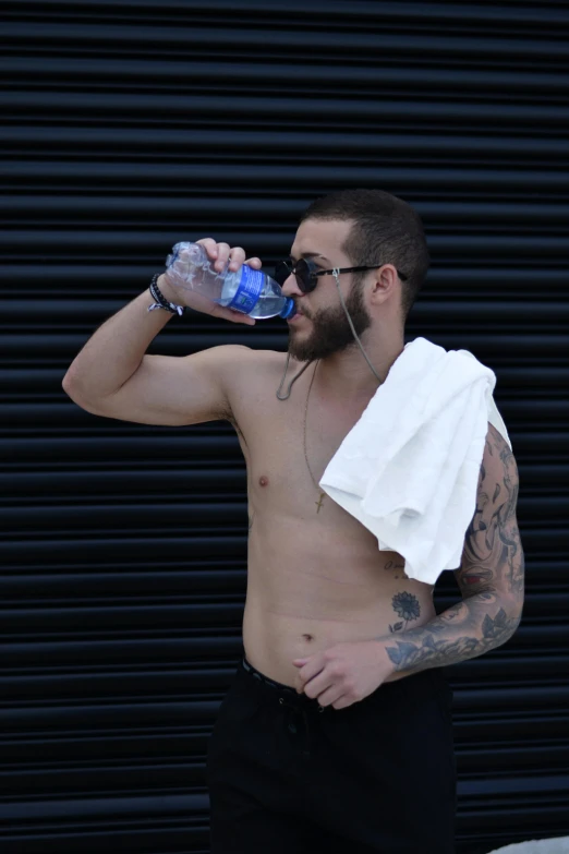 shirtless man drinks from water bottle outside
