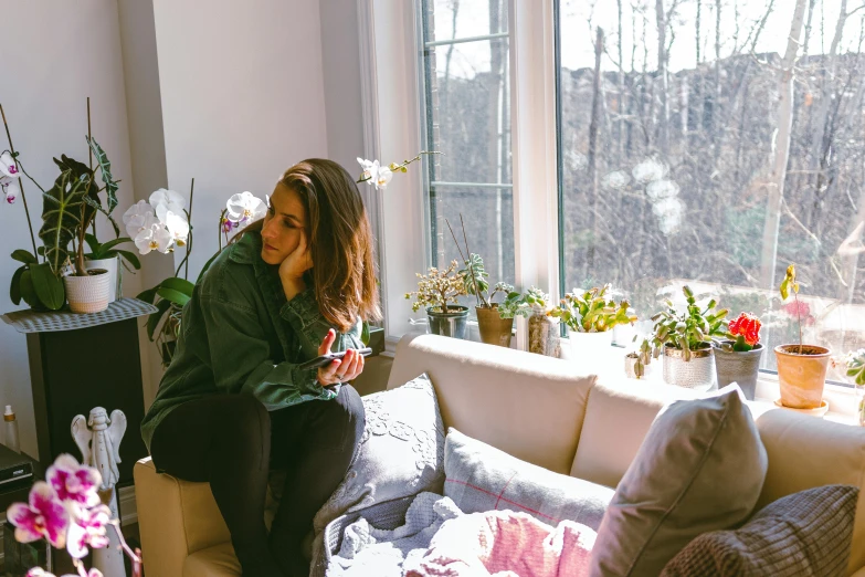 a woman sitting on a couch with plants outside a window