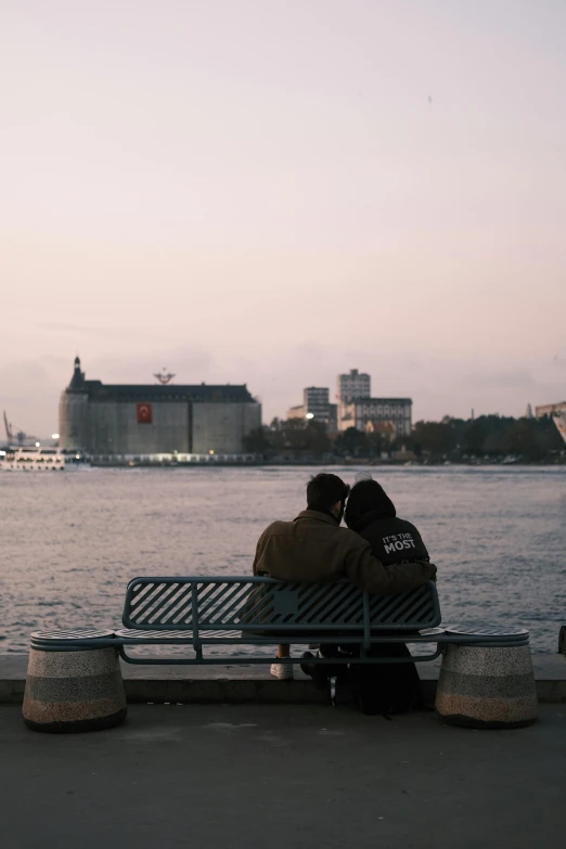 two people sitting on a bench by the river