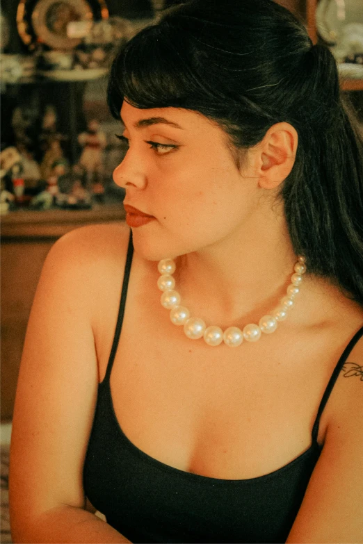 a woman is wearing a black dress and pearls necklace