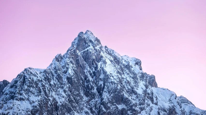 the snow covered mountain top is silhouetted against the pink sky