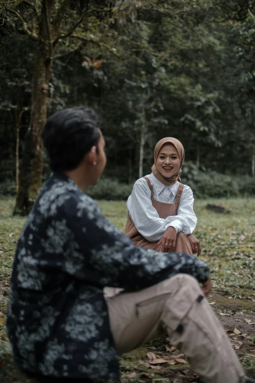 a woman in head scarf sitting on the ground in forest