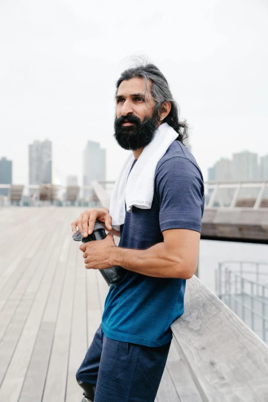 a man with long hair and a beard stands at a pier