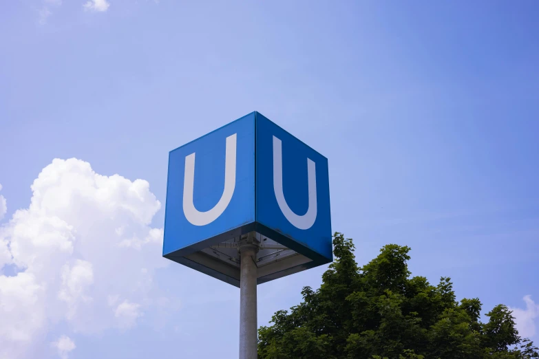 an unotalled blue sign stands on a tall pole under a partly cloudy sky