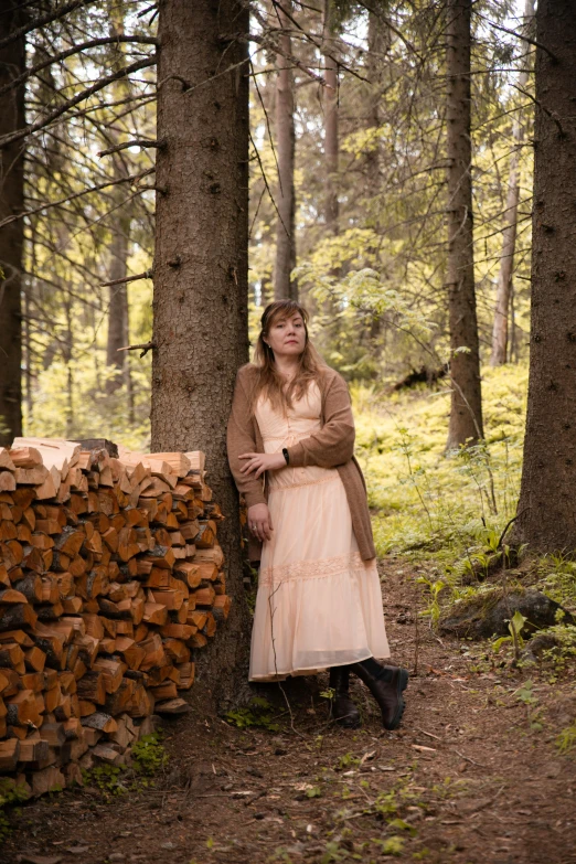 a woman in a dress leaning against a tree in a forest