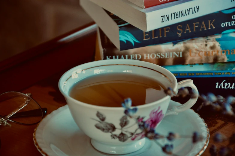 a cup of tea with a spoon in it sits next to three books and some glasses