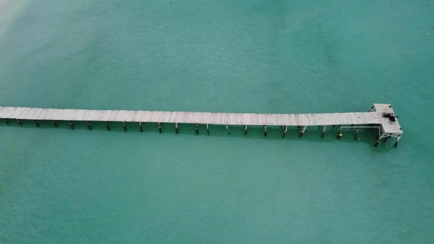 a long white dock on the ocean with a motorboat