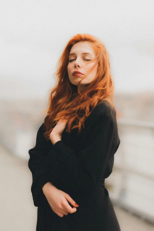 a young woman with red hair and a black dress is leaning on a rail