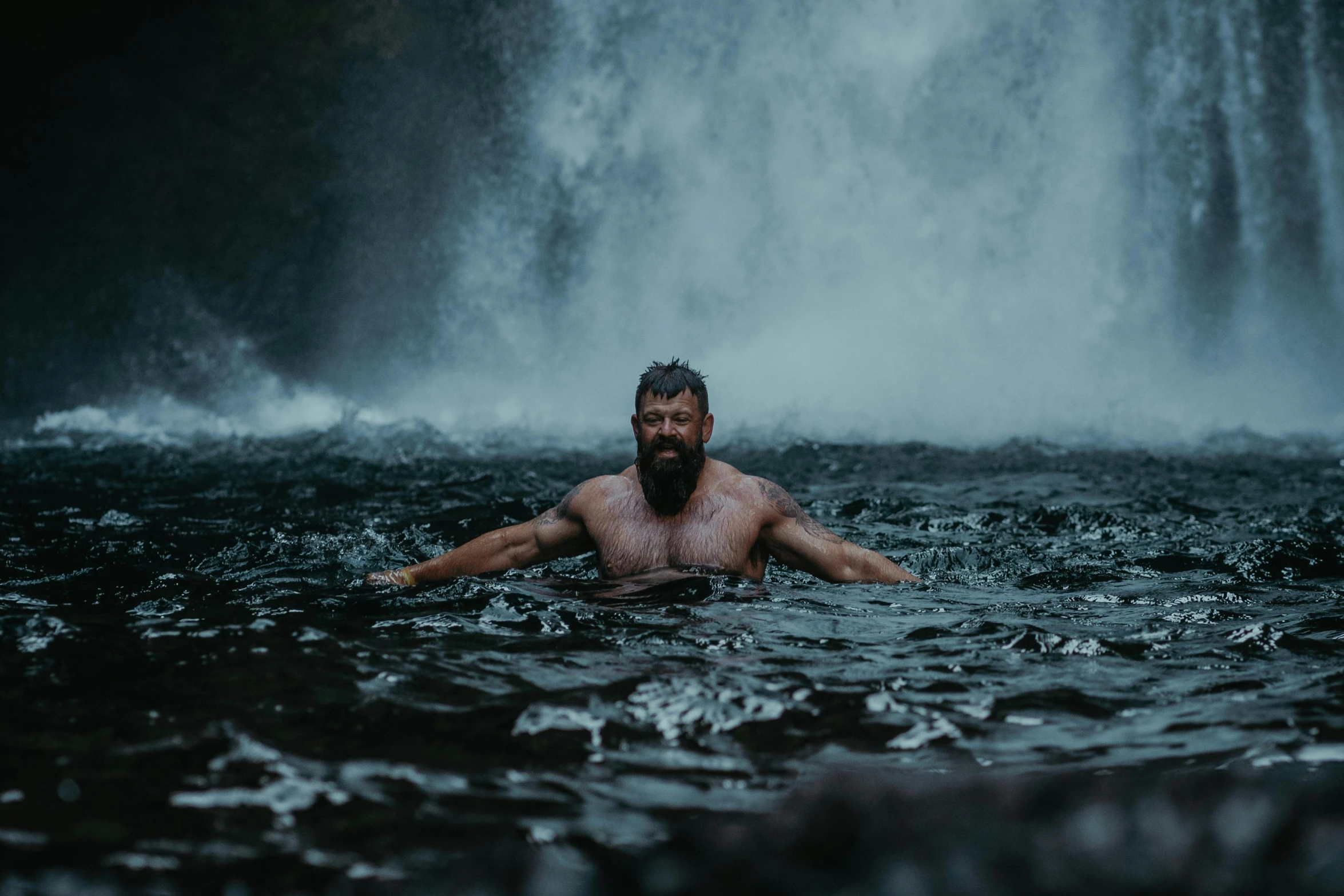 man in body of water near large waterfall