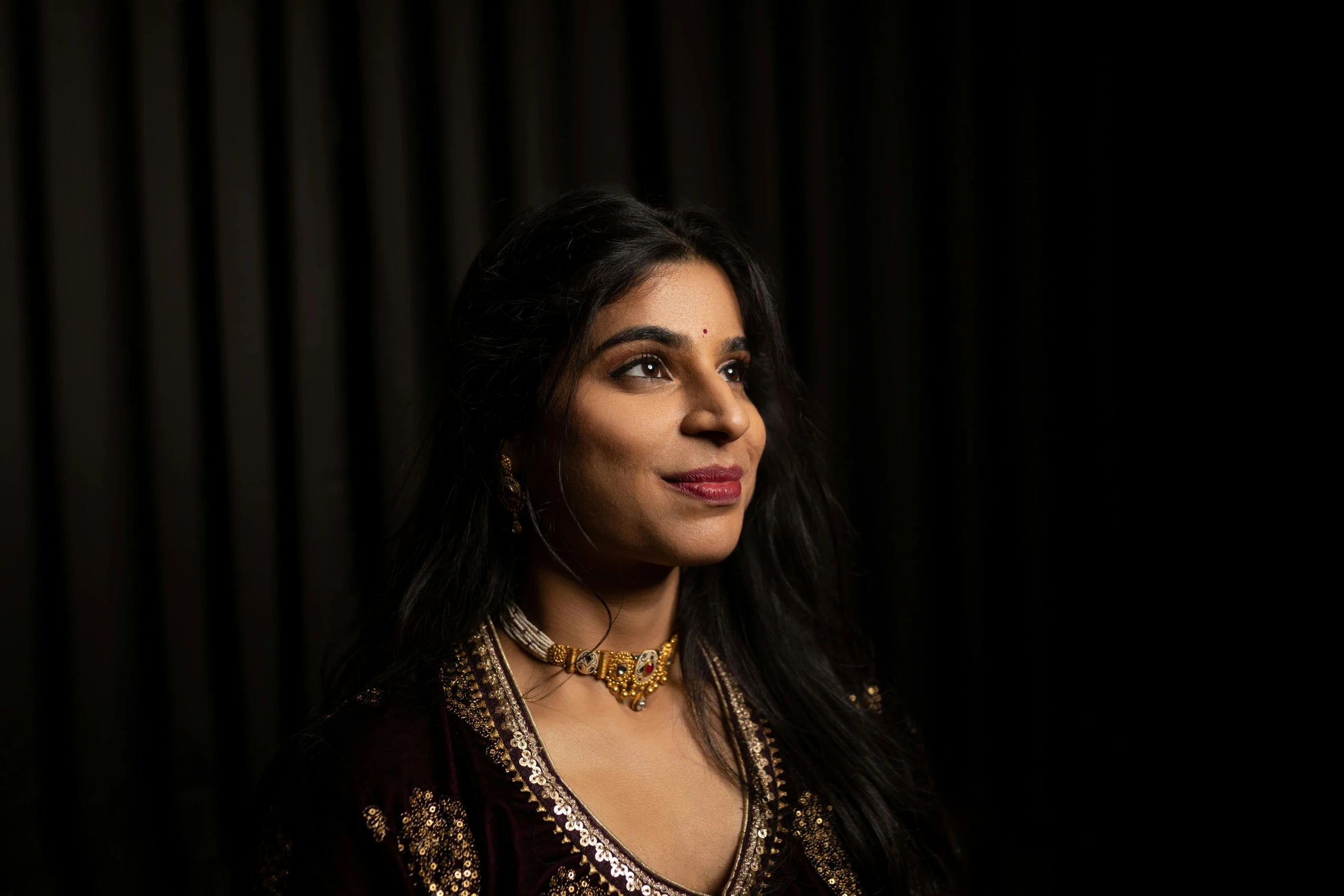 a young woman wearing a gold and silver blouse looking up