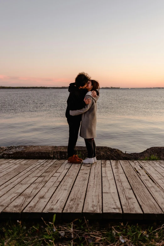 two women hugging at a pier in front of the water