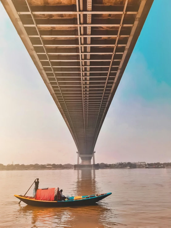 a person on a small boat beneath an ocean bridge