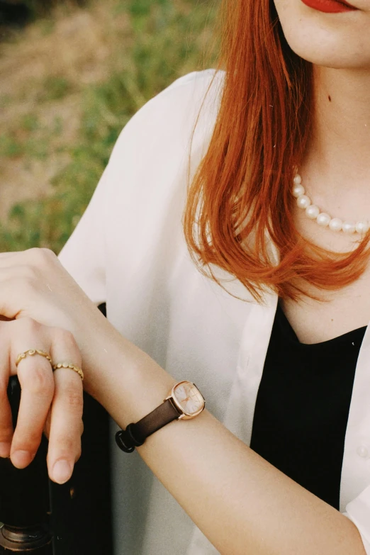 woman's red hair wearing a pearl celet holding onto a wine bottle