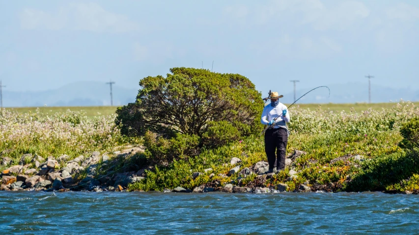 a man fishing in the water on an island with rocks and plants