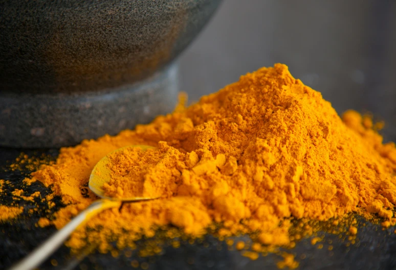 a spoon that is next to some tumeric and spices