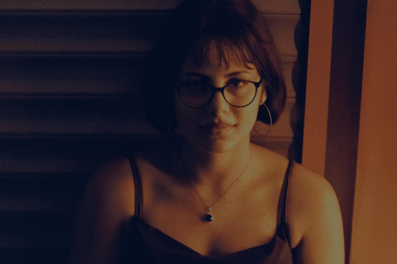 a woman wearing glasses sitting on a chair in the dark