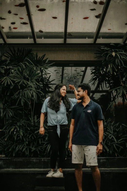 couple posing for camera in front of a wall of plants