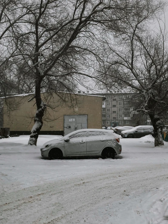 a city street with snow covered cars and trees