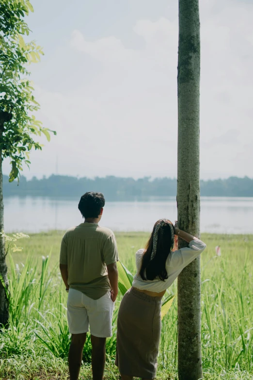 a couple looking at the water while they are standing by a tree